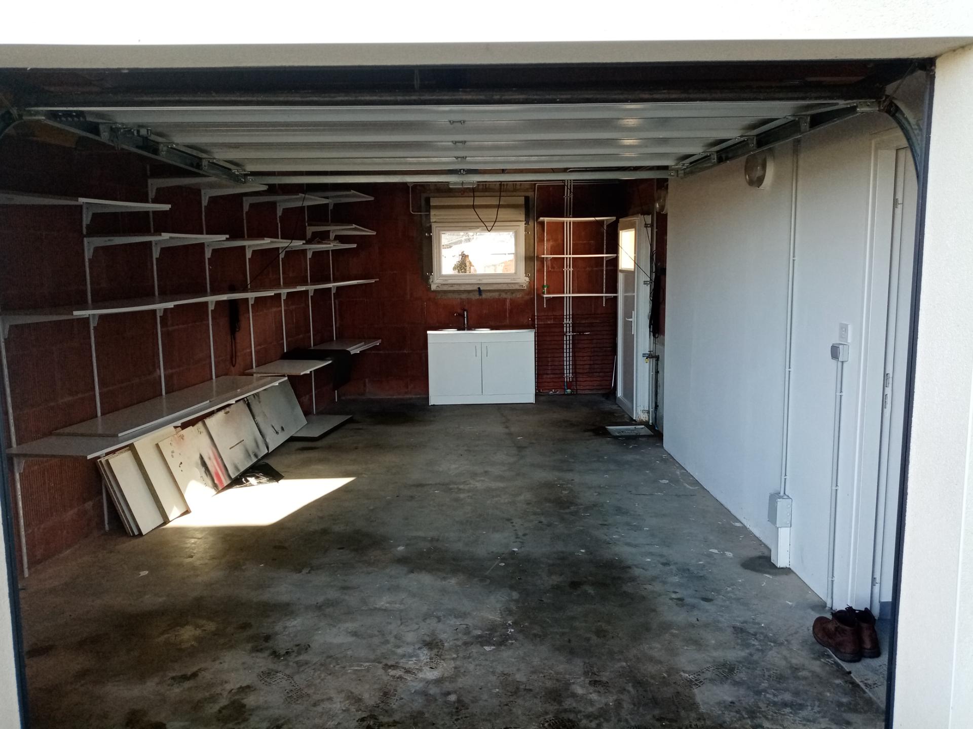 Garage vidé et balayé — étagères, sol béton, fenêtre dépoussiérée